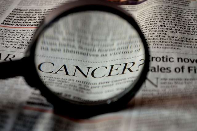 magnifying glass on newspaper enlarging the word cancer for cancer awareness