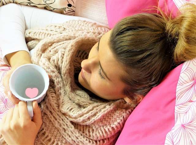 girl at bed rest during cold and flu with cup of hot water